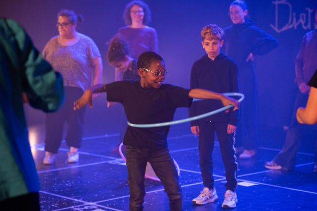 Sur scène, un jeune garçon souriant joue du cerceau façon hula hoop